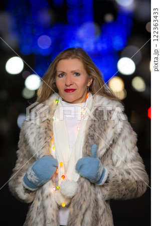 Portrait of a beautiful middle-aged woman in a fur coat in the lights of the evening city. 122363433