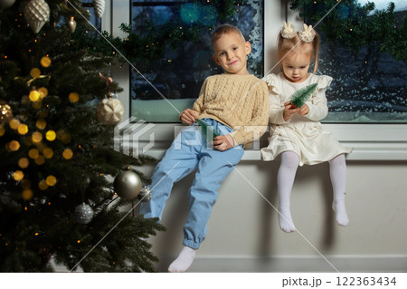 Happy children brother and sister are sitting on the window of the Christmas room. 122363434