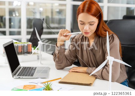 Ginger young woman working in the office on a new project of wind farm Ginger young woman working in the office on a new project of wind farm 122365361
