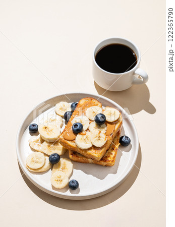 Peanut butter toast with banana and blueberry on a plate on a beige background with a cup of coffee 122365790