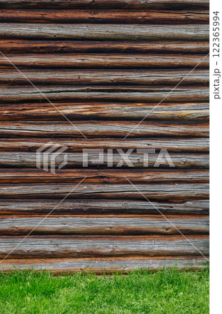Weathered wooden logs creating rustic wall, revealing traditional russian architectural style amid verdant grassy landscape 122365994