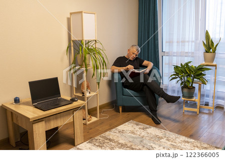 Man sitting in the cozy corner in the apartment on comfortable arm chair. 122366005