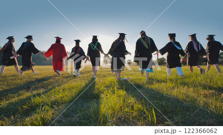 Group of graduates in robes walking hand in hand into the sunset in a meadow Group of graduates in robes walking hand in hand into the sunset in a meadow 122366062