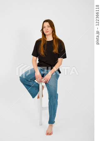 Young woman sitting on a stool with a casual pose in a bright studio setting 122366118