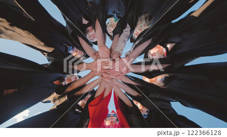Recent graduates in cap and gown join hands in a circle 122366128