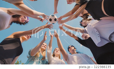 High school students showing unity and teamwork as they reach for a soccer ball under the summer sky, symbolizing friendship and love for the sport High school students showing unity and teamwork as they reach for a soccer ball under the summer sky, symbolizing friendship and love for the sport 122366135