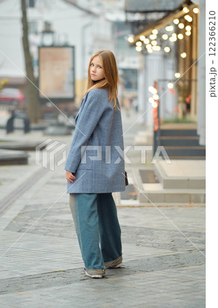 Woman in blue coat and wide pants strolls in an urban area during early evening light 122366210