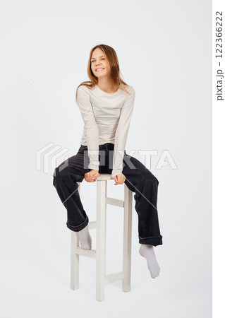 Young person sitting on a white stool and smiling against a minimal background Young person sitting on a white stool and smiling against a minimal background 122366222