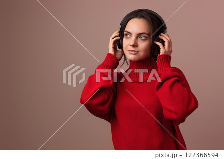 Happy woman wearing red sweater and headphones enjoying listening music on pink background. Happy woman wearing red sweater and headphones enjoying listening music on pink background. 122366594