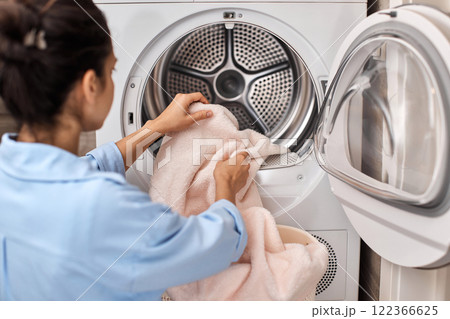 woman put pastel cotton towel in automatic washing machine with open door woman put pastel cotton towel in automatic washing machine with open door 122366625