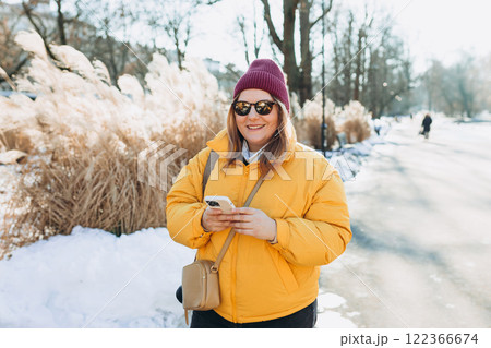 Young stylish 30s woman in sunglasses writes message on smartphone walking on city street. Urban lifestyle concept. Winter time. Charming female wearing stylish outfit chatting online Young stylish 30s woman in sunglasses writes message on smartphone walking on city street. Urban lifestyle concept. Winter time. Charming female wearing stylish outfit chatting online 122366674