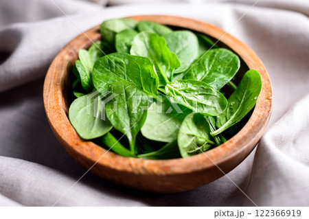 Heap of baby spinach leaves with water drops in a wooden bowl Heap of baby spinach leaves with water drops in a wooden bowl 122366919