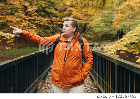 Blonde male with backpack pointing finger outdoors, he hiking on woodland. Active lifestyle concept. Trip, travel and people banner. High quality photo Blonde male with backpack pointing finger outdoors, he hiking on woodland. Active lifestyle concept. Trip, travel and people banner. High quality photo 122367453