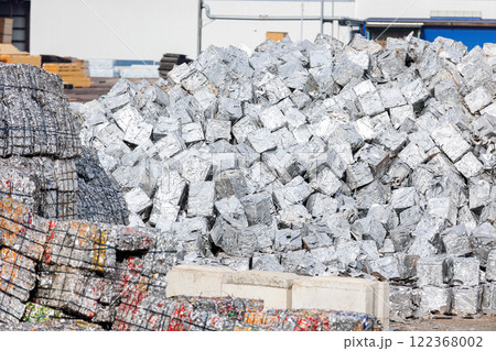 tacks of pressed aluminum cubes glisten in bright light, hinting at large-scale recycling operations. Reflective surfaces highlight an industrial push toward sustainability and efficient resource use 122368002