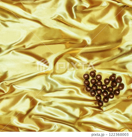 Seamless heart-shaped chocolate candy pattern on yellow silk fabric background. 122368003