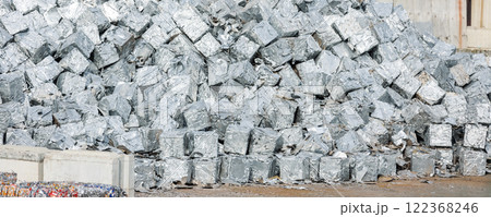 tacks of pressed aluminum cubes glisten in bright light, hinting at large-scale recycling operations. Reflective surfaces highlight an industrial push toward sustainability and efficient resource use 122368246