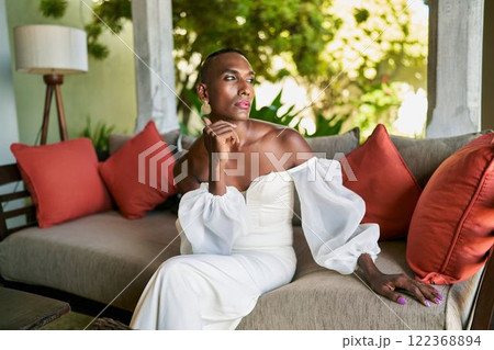 Gender fluid person in white dress sits on villa patio. Lgbtq wedding themes, elegant fashion, inclusive diversity. Modern bride celebrates unique identity, embraces style in serene garden. 122368894