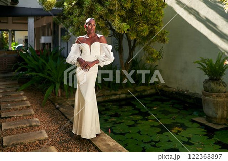 Elegant person in white dress stands on villa path by lily pond. Gender fluid black bride embodies modern inclusive fashion by tropical greenery. Unique style for weddings and events. Elegant person in white dress stands on villa path by lily pond. Gender fluid black bride embodies modern inclusive fashion by tropical greenery. Unique style for weddings and events. 122368897