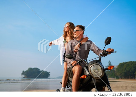 Couple rides motorbike on beach. Woman enjoying breeze, man steering. Romantic getaway, travel freedom, exploring nature together. Sunset adventure, love journey. Couple rides motorbike on beach. Woman enjoying breeze, man steering. Romantic getaway, travel freedom, exploring nature together. Sunset adventure, love journey. 122368905