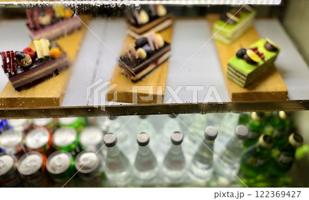 Portions of puff pastry with cream and chocolate, yellow cakes with red raspberries, blackberries, blueberries on wooden stands at restaurant. There are cans and bottles of lemonade on the bottom 122369427