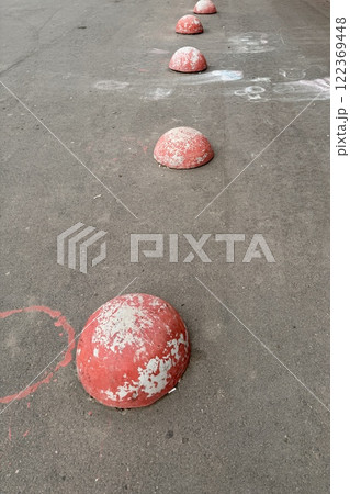 Red restrictive hemispheres on the asphalt road in the parking area of the car and the pedestrian area of walking people at the street. Area for foot people 122369448