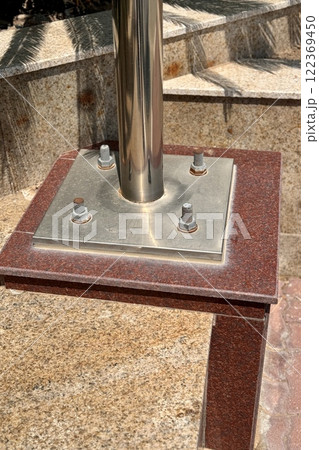 Metal pillar fastened to basement with different anchor bolts and nuts. The support of the iron black pillar on a green lawn in city center Metal pillar fastened to basement with different anchor bolts and nuts. The support of the iron black pillar on a green lawn in city center 122369450