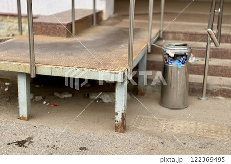 Overflowing trash can and scattered garbage on a sidewalk next to stairs next to supermarket Overflowing trash can and scattered garbage on a sidewalk next to stairs next to supermarket 122369495