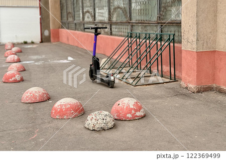 Red restrictive hemispheres on the asphalt road in the parking area of the car and the pedestrian area of walking people at the street. There is an unknown parked black scooter in front of them Red restrictive hemispheres on the asphalt road in the parking area of the car and the pedestrian area of walking people at the street. There is an unknown parked black scooter in front of them 122369499