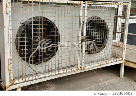 Two refrigeration fans for industrial cold rooms of supermarket. Air coolers refrigeration evaporators installed on ground have metal wire crate, closed doors with hinged metal lock for maintenance Two refrigeration fans for industrial cold rooms of supermarket. Air coolers refrigeration evaporators installed on ground have metal wire crate, closed doors with hinged metal lock for maintenance 122369502