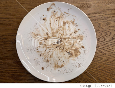 A dirty white porcelain plate after a delicious meal is on a brown table in a restaurant. Leftover food. Close-up 122369521