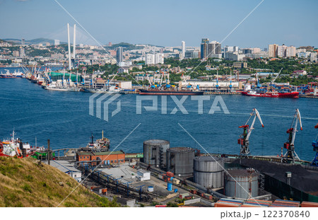 Cargo vessels traversing vladivostok's harbor, passing under golden horn bay bridge with industrial cranes preparing for loading operations Cargo vessels traversing vladivostok's harbor, passing under golden horn bay bridge with industrial cranes preparing for loading operations 122370840