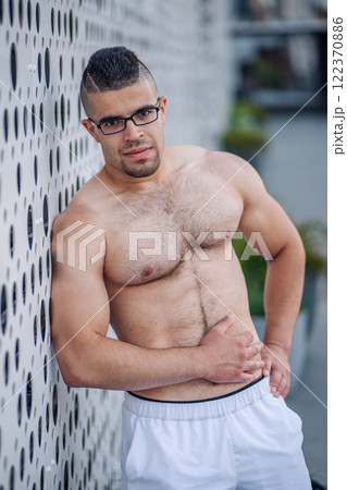 Shirtless sportsman with glasses and a striking mohawk hairstyle posing confidently against a modern perforated metal wall in russia Shirtless sportsman with glasses and a striking mohawk hairstyle posing confidently against a modern perforated metal wall in russia 122370886