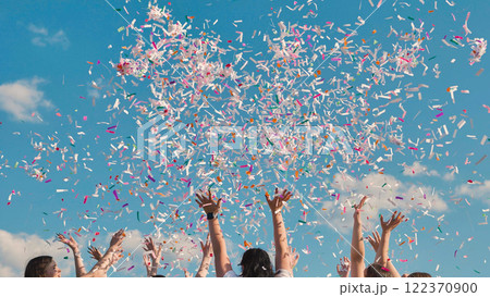 High school graduates joyfully throwing colorful confetti in the air under a clear blue sky High school graduates joyfully throwing colorful confetti in the air under a clear blue sky 122370900