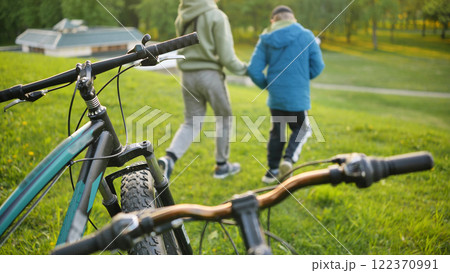 Children walking hand in hand across grassy park, abandoned bicycles nearby 122370991