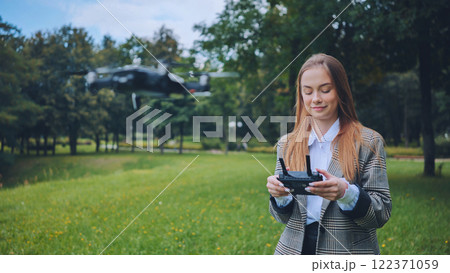 Businesswoman navigating an unmanned aerial vehicle in a park, showcasing innovation and technology in a natural setting 122371059