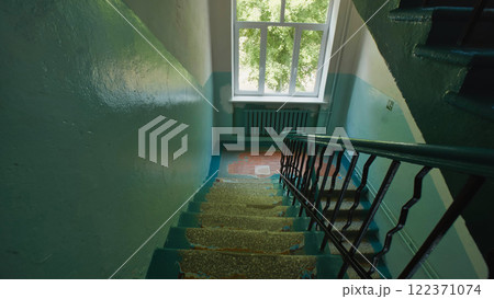 Abandoned school building staircase with peeling paint, sunlight streaming through window at the top 122371074