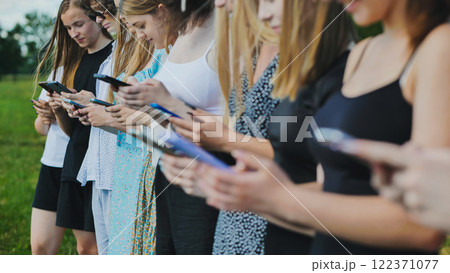 Teenagers in a line outdoors during summer, using smartphones to connect and communicate 122371077