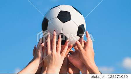 Many hands holding a soccer ball against a blue sky, symbolizing teamwork, friendship, and sportsmanship in school 122371080