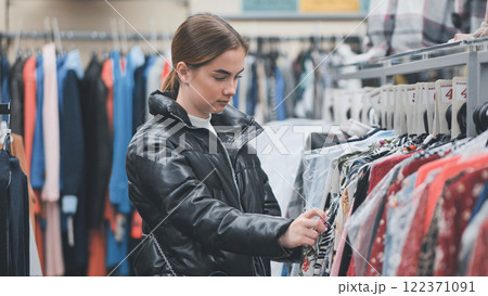 Shopper browsing trendy clothing, carefully examining garments on racks and weighing fashion choices in stylish retail environment 122371091