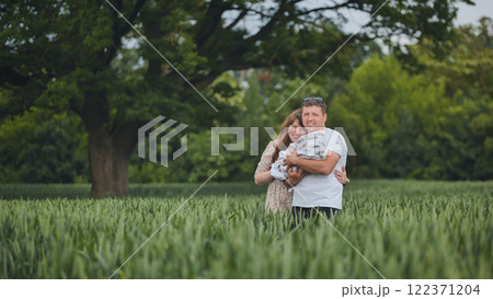 Parents holding their newborn baby in a green wheat field under a big tree, enjoying a peaceful family moment in nature 122371204