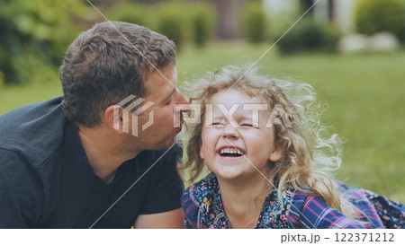 Loving dad tenderly kissing giggling daughter's cheek, sharing warm moment during outdoor family gathering 122371212