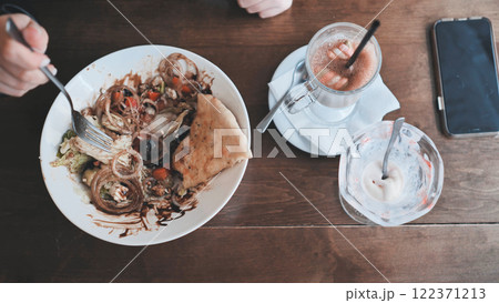 Person eating fresh salad, sipping hot drink beside smartphone, pita bread and sweet treat at cozy cafe table 122371213