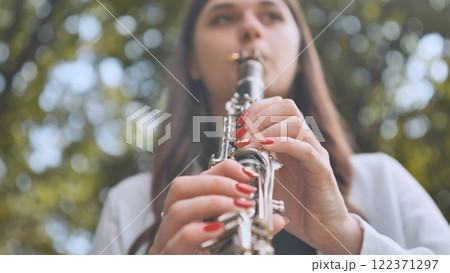 Female musician performing clarinet amid lush greenery, expressing musical passion through melodic outdoor performance Female musician performing clarinet amid lush greenery, expressing musical passion through melodic outdoor performance 122371297