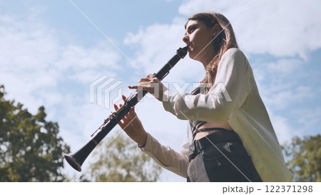 Georgian girl playing the clarinet in a sunlit park, savoring the joy of music amidst the beauty of nature and summer's warmth Georgian girl playing the clarinet in a sunlit park, savoring the joy of music amidst the beauty of nature and summer's warmth 122371298