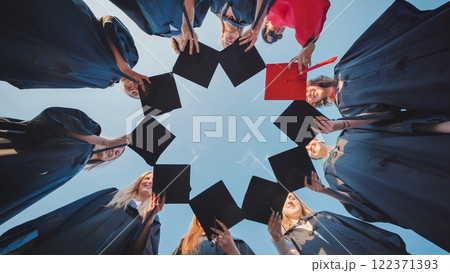 Students in graduation attire come together to form a star shape and gaze skyward in celebration 122371393