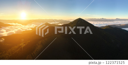 Aerial view of amazing scenery with foggy dark mountain peak covered with forest pine trees at autumn sunrise. Beautiful wild woodland with shining rays of light at dawn Aerial view of amazing scenery with foggy dark mountain peak covered with forest pine trees at autumn sunrise. Beautiful wild woodland with shining rays of light at dawn 122371525