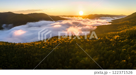 Aerial view of amazing scenery with foggy dark mountain forest pine trees at autumn sunrise. Beautiful wild woodland with shining rays of light at dawn Aerial view of amazing scenery with foggy dark mountain forest pine trees at autumn sunrise. Beautiful wild woodland with shining rays of light at dawn 122371526