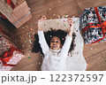 Happy cute black girl playing with stretched hands by colorful confetti on floor with Christmas gift boxes 122372597