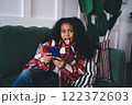 Playful black girl using smartphone while sitting on sofa 122372603