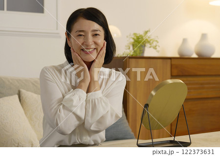 夜のリビングで顔に化粧水を塗る50代の女性 122373631